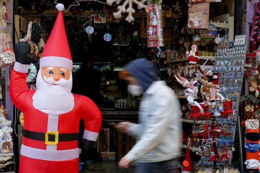 Un uomo con la mascherina passa accanto a un pupazzo di Babbo Natale