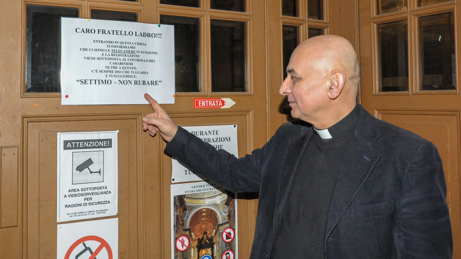 Don Antonio indica un cartello affisso all'entrata della chiesa per scoraggiare i ladri