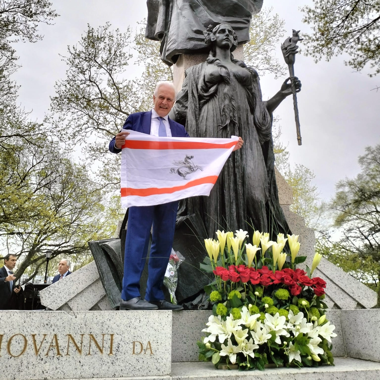Il presidente Giani con la bandiera della Regione Toscana davanti al monumento dedicato a Giovanni Da Verrazzano a New York