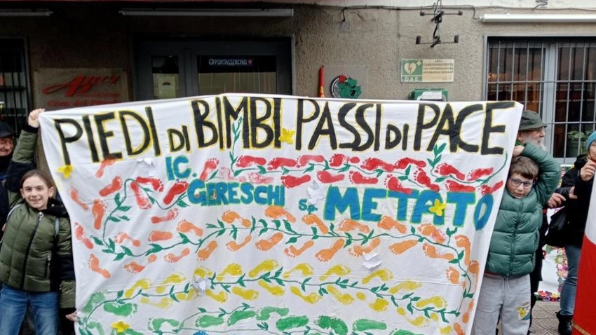 Sopra i piccoli tutti insieme per la pace, sotto un disegno che rappresenta la guerra