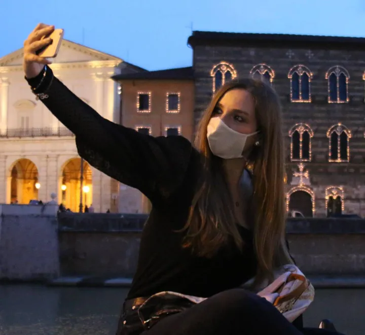 Una ragazza mentre si fa un selfie sulle spallette dell’Arno. Sotto la medaglia in regalo