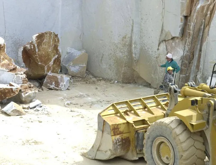 Operatori al lavoro all’interno di una cava di marmo mentre utilizzano mezzi e strumenti tecnici per l’estrazione del prezioso materiale