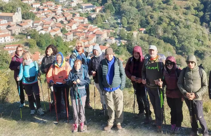 Escursionisti durante un trekking in montagna e alle spalle il paese di Sassalbo