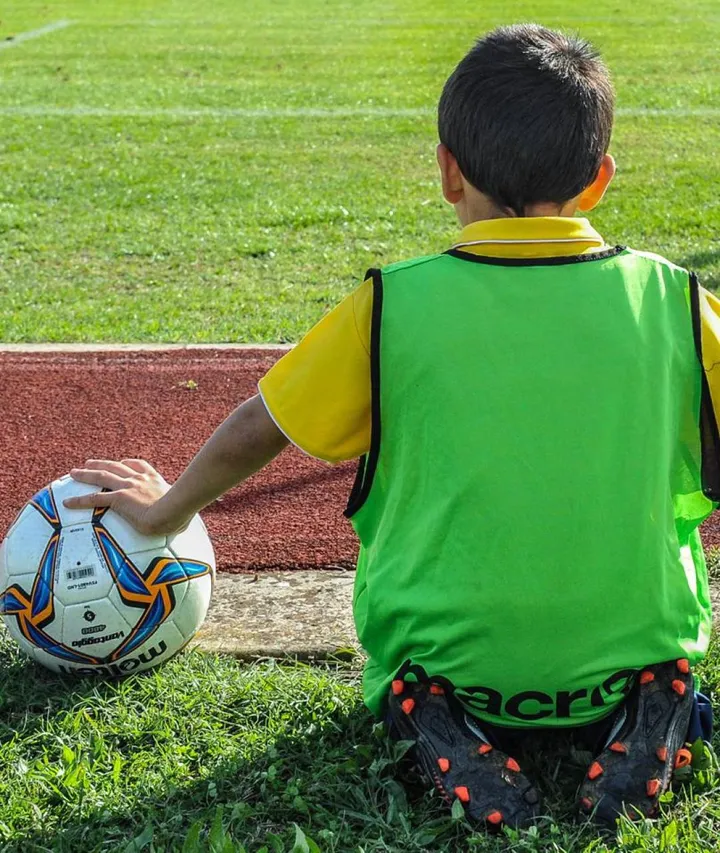 Un piccolo calciatore a bordo campo guarda i compagni giocare (foto d’archivio)
