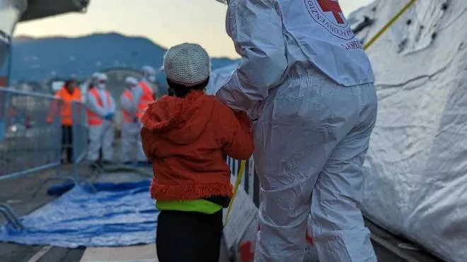 Un ragazzino accompagnato verso la salvezza da un operatore della Croce rossa subito dopo lo sbarco dalla Geo Barents